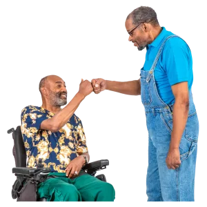 a person with a beard, sitting in a wheelchair fist bumps another person with a beard who is standing up.