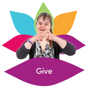 Woman with Down syndrome making a heart gesture with her hands in front of a colourful lotus flower.